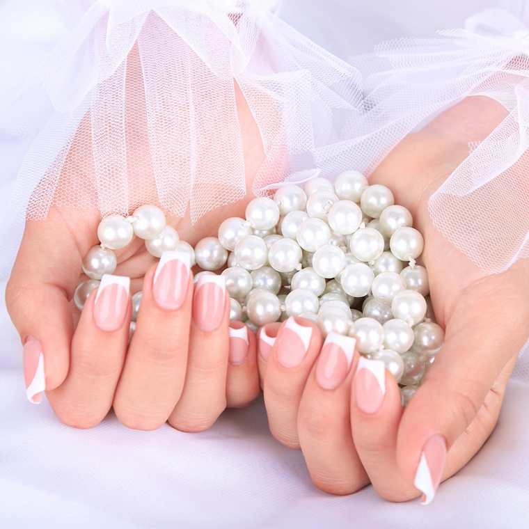 Unghie gel french bianco, collana di perle in mano della sposa con un velo bianco 