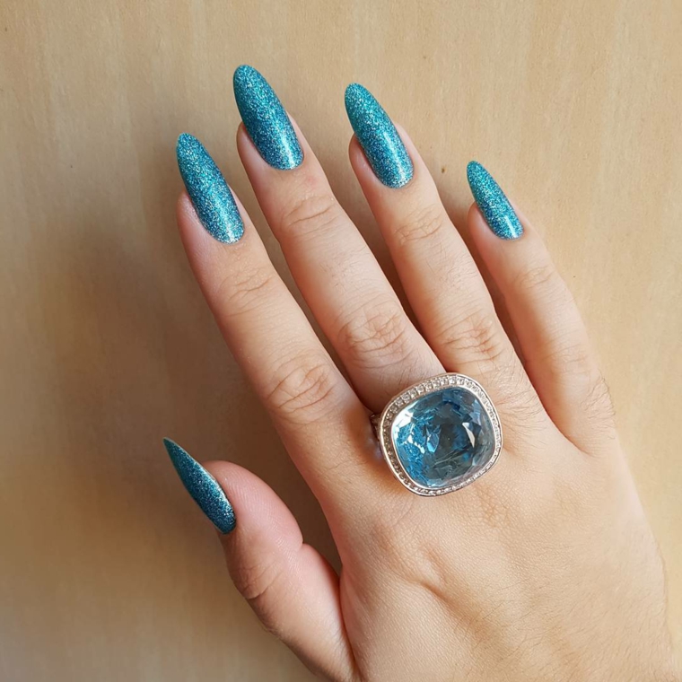 Ricostruzione unghie a mandorla, smalto ruvido di colore azzurro glitterato, accessori donna e un anello con diamante della stessa tonalità di colore 