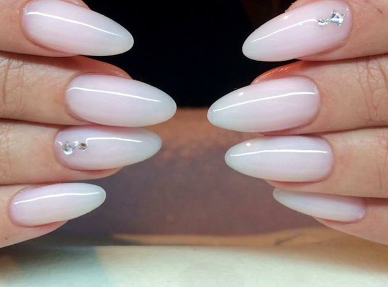 Smalto rosa bianco con applicazione di brillantini sul dito anulare per una manicure perfetta 