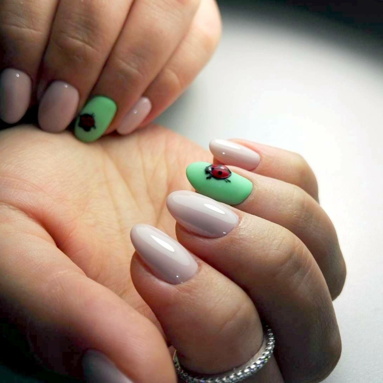 Decorazione con coccinella su una base di colore verde, unghie corte di colore beige a forma di mandorla 