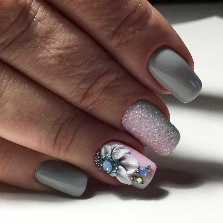 La mano di una donna con smalto di colore grigio, unghie opache con disegni di fiori ed effetto sugar