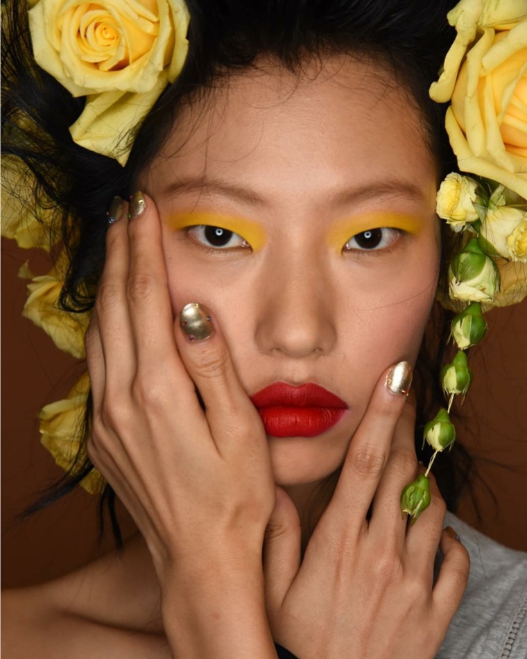 Donna con fiori in testa, smalto color argento lucido, unghie gel semplici, ombretto giallo