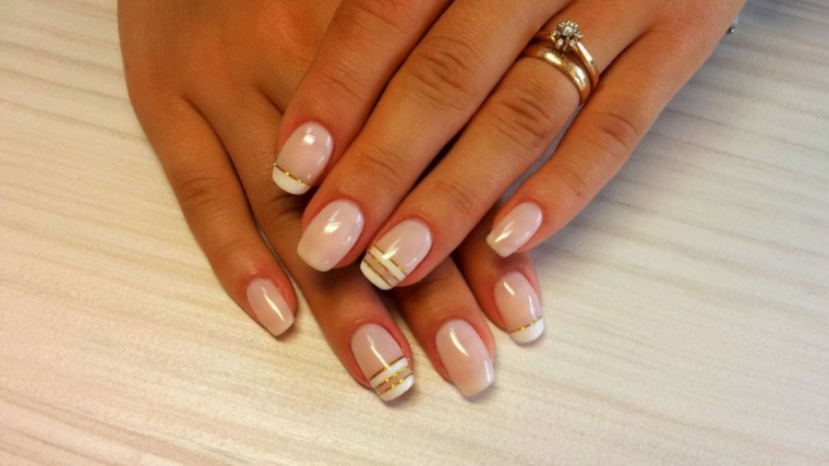 nail art creativa e chic, unghie color cipria con alcune decorazioni orizzontali bianche e oro