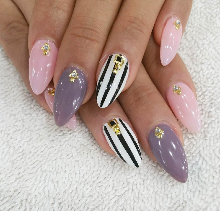 Unghie a stiletto di colore viola e rosa, accent nail bianco con linee nere e decorazioni con brillantini 