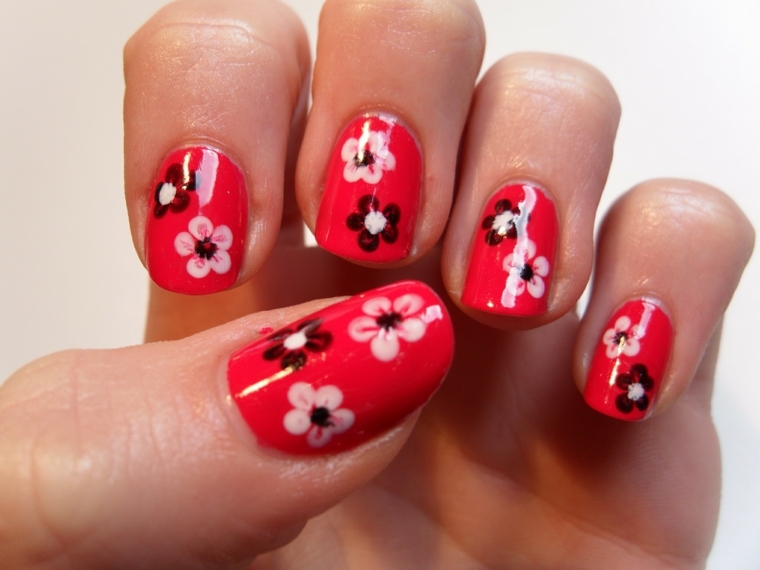 unghie rosse decorate, una proposta con dei piccoli fiori bianchi e neri