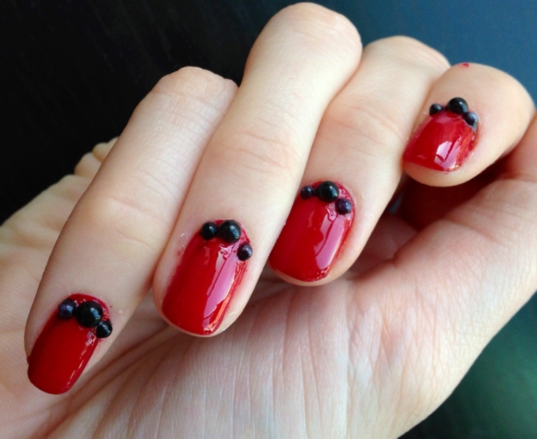 gel rosso, una manicure in tinta unita brillante e palline decorative applicate sotto la cuticola