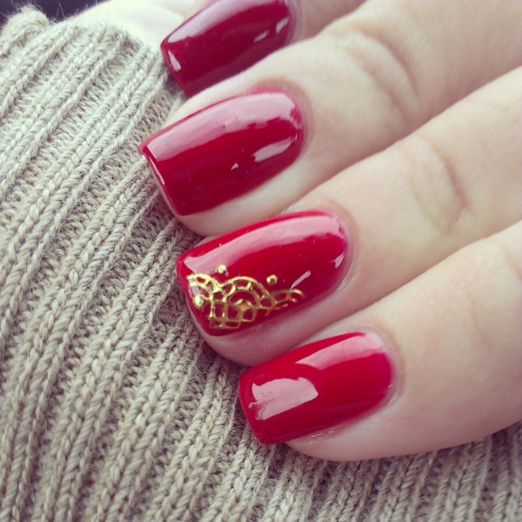 unghie dipinte con uno smalto rosso rosso brillante e anulare decorato con un disegno dorato 