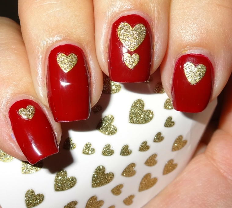 unghie laccate con smalto rosso e decorate con dei cuoricino dorati