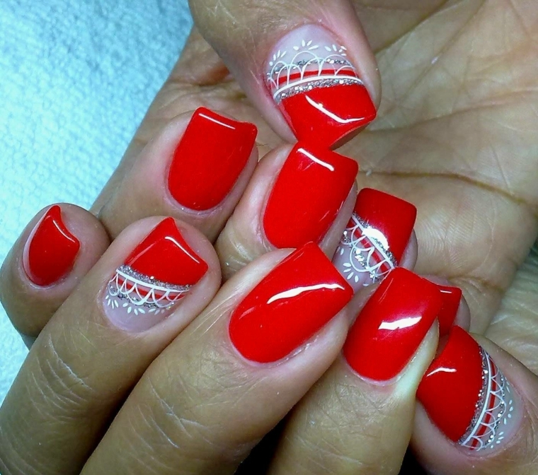 unghie rosso, una manicure realizzata con uno smalto rosso chiaro brillante e decorazioni bianchi e argento
