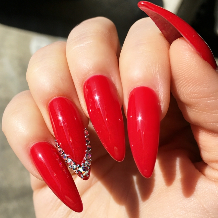 unghie rosse gel, una manicure a stiletto con dei glittert applicati a v sull'anulare