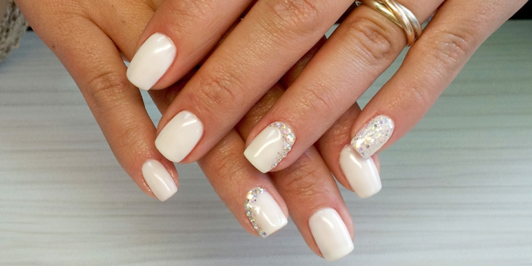 Decorazioni con brillantini per delle unghie di colore bianco dipinte con smalto gel 